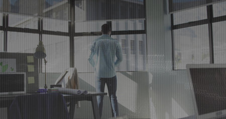 Standing architect wearing shirt and trousers gazing through windows in office, with monitor. Modern, professional, creative, minimalist, urban, innovative, workspaceの写真素材