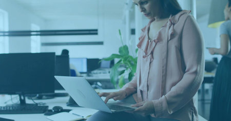 Sitting businesswoman typing on laptop on desk edge at open office, smartphone notebook, copy space....
