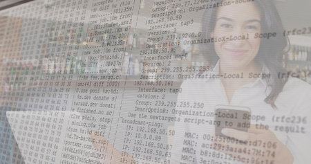 Working IT professional holding smartphone and typing on laptop at office desk, with code overlay. Technology, cybersecurity, digital, innovation, professional, modern, connectivityの写真素材