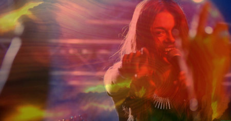 Performing singer in dark gear pointing to viewer on stage, with mic, necklace, lights, copy space. Concert, performance, illumination, entertainment, stagecraft, dynamic, acousticの写真素材