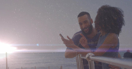 Leaning couple viewing smartphone on metal railing overlooking ocean horizon at sunset, copy space. Romantic, coastal, leisure, scenic, serene, connection, duskの写真素材