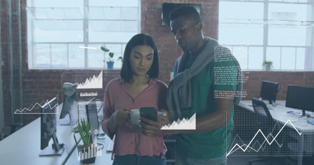 Two tech colleagues reviewing smartphone data charts in open-plan office, holding coffee mug....