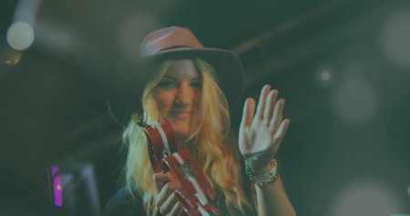 Musician shaking red tambourine and waving under stage lights, with wide-brimmed hat and bracelets. Performer, concert, performance, stage, entertainment, energetic, vibrantの写真素材