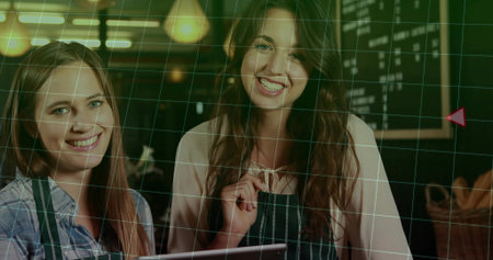 Holding digital tablet and adjusting striped apron, two baristas standing behind counter at cafe. Coffee shop, teamwork, hospitality, rustic, modern, branding, service industryの写真素材