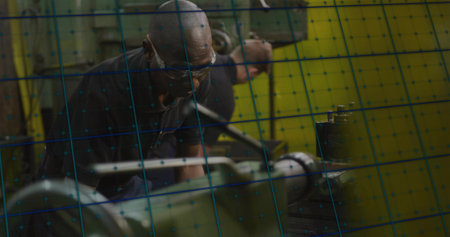 Technician wearing safety glasses adjusting workpiece in workshop, with metal cage and lathe....
