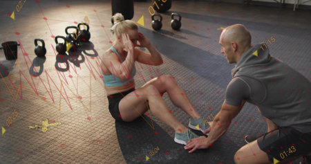 Woman in athletic wear doing sit-ups on gym mat, with coach support, kettlebells and punching bag....