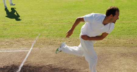 Bowling cricketer delivering ball on cricket pitch, with crease lines and vibrant outfield. Athletic, sports, competition, outdoor, dynamic, performance, trainingの写真素材