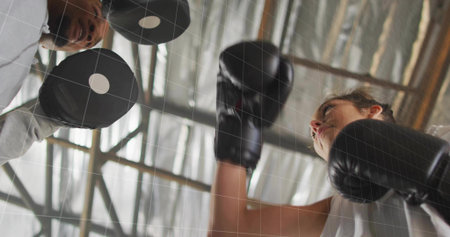 Trainee in black gloves delivering jab in gym, coach wearing baseball cap holding focus mitts. Athletic, training, strength, determination, performance, industrial, dynamicの写真素材
