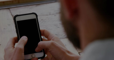 Holding mid adult man's hands positioning smartphone over whitewashed wooden table, protective case....