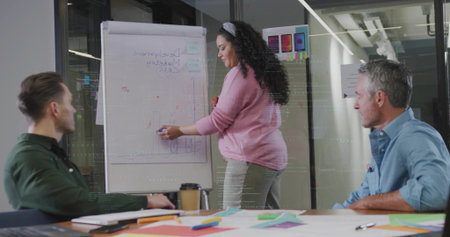 Woman in pink sweater sketching bar graph at flip chart in conference room, with blue marker....
