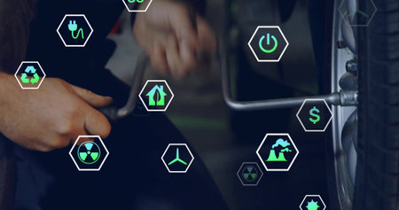 Mechanic in coveralls applying torque on car wheel in workshop, with lug wrench and eco symbols. Automotive, maintenance, industrial, eco-friendly, renewable, sustainable, manual workの写真素材