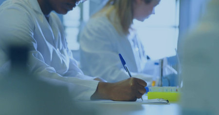 Documenting African American scientist writing with pen on clipboard at lab bench, test tube rack. Research, collaboration, innovation, modern, professional, analytical, scientificの写真素材