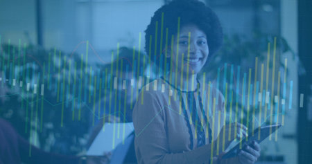 Woman in tan sweater and lanyard holding tablet and analyzing data graphs in office with laptops. Collaboration, analytics, productivity, modern, teamwork, technology, workspaceの写真素材