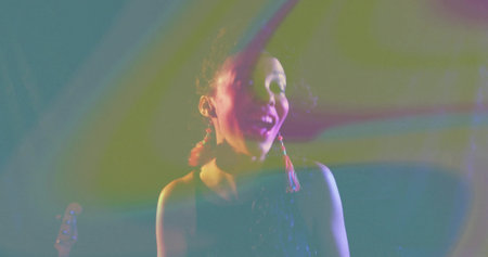Singing performer wearing sequin top onstage, with colored lights, smoke haze and guitar headstock....