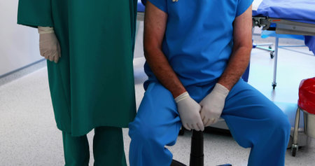 Nurse and surgeon preparing tools in operating room, with blue table, gloves and red waste bin. Clinical, teamwork, sterile, healthcare, professional, precision, hospitalの写真素材
