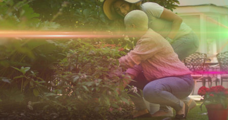 Two women tending flowering shrub in backyard, with red potted flowers and patio chairs and table. Nature, friendship, outdoor, leisure, vibrant, tranquility, botanicalの写真素材