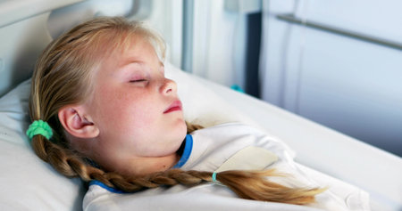 Female child patient sleeping on hospital bed, with metal rails and white blanket. Pediatric, healthcare, medical, healing, therapy, wellness, comfortの写真素材