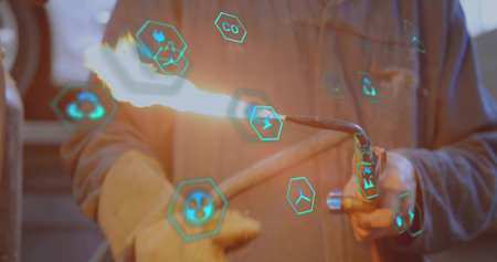 Technician wearing gloves and jacket holding torch emitting flame in metal workshop, with AR icons....