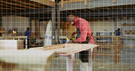 Sanding carpenter wearing red shirt and goggles smoothing plank in workshop, with portable sander....