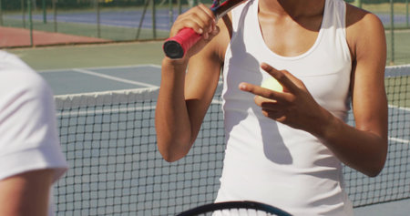 Signaling female tennis player holding racket near net on outdoor court, with fence and court lines. Athletics, competition, sport, fitness, teamwork, determination, energeticの写真素材