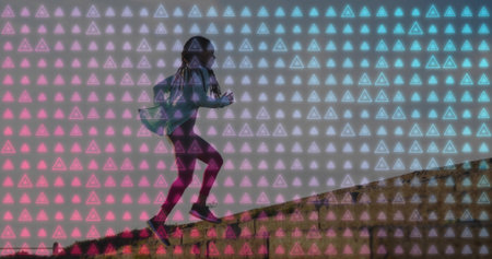 Running woman in jacket and leggings climbing grassy hill at dawn, with glowing triangle overlay. Fitness, outdoor activity, digital art, futuristic, motion, vitality, adventureの写真素材