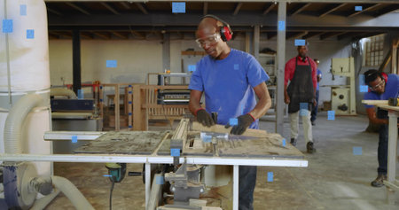 Operating carpenter feeding wooden board through table saw in workshop, with sawdust and gloves....