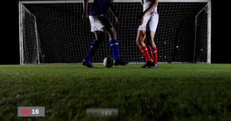 Dueling players under lights, with soccer ball, goal net, red record icon overlay, on-screen timer. Athletic, competition, nighttime, outdoor, sport, intensity, focusの写真素材