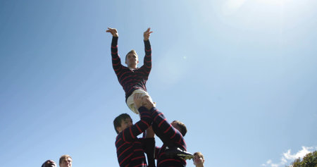 Hoisting rugby player in line-out drill wearing jerseys, cleats on grassy field, with lens flare. Athletic, teamwork, dynamics, outdoor, vigorous, sport, competitionの写真素材
