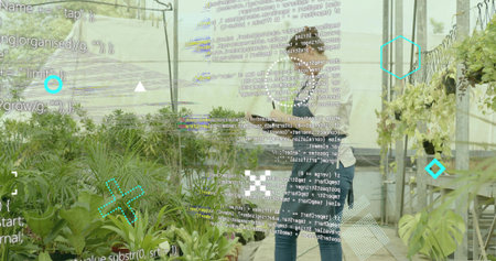 Holding tablet, horticultural workers monitoring potted plants in greenhouse, with data overlay. Botanical, agriculture, precision, sustainability, contemporary, industry, collaborationの写真素材