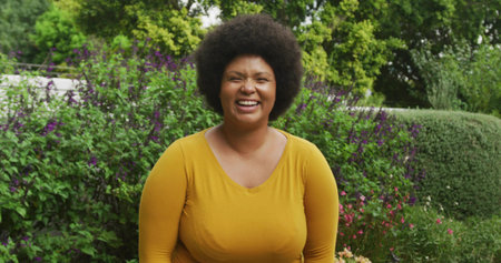 Smiling woman wearing mustard yellow top standing in garden, surrounded by trimmed hedge and shrubs. Nature, outdoor, vibrant, serenity, wellness, leisure, horticultureの写真素材