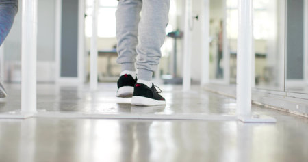 Walking adult male wearing grey sweats, white socks, black sneakers in studio with mirror, barre. Footwear, athletic, gym, movement, reflection, daylight, corridorの写真素材