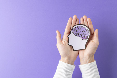 Composition of hands holding head silhouette with purple brain on purple background, with copy...