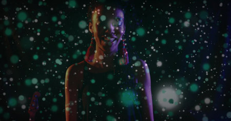 Performing artist wearing red tassel earrings standing on stage, under green and white light spots. Theater, spotlight, performance, stage, glamour, entertainment, nightの写真素材