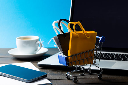 Composition of shopping cart with bags and laptop on blue background. Retail, shopping and black friday concept.の写真素材