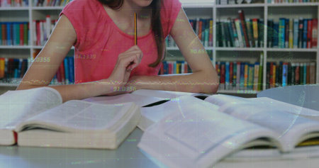Pondering teenage girl in pink top holding pencil under chin at library table, with open textbooks....