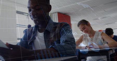 Smiling male student holding tablet at classroom desks, with notebooks and data overlay graphics. Education, collaboration, innovation, digital, youth, learning, technologyの写真素材