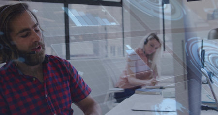 Speaking man wearing plaid shirt and headset at call center desk, monitors, overlay, copy space. Collaboration, communication, technology, professional, teamwork, modern, corporateの写真素材