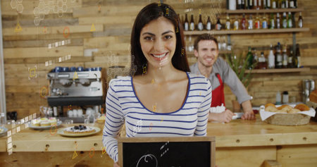 Smiling female cafe staff holding blank chalkboard sign in cafe, with pastries and coffee maker. Coffee shop, hospitality, artisanal, rustic, teamwork, community, warmの写真素材
