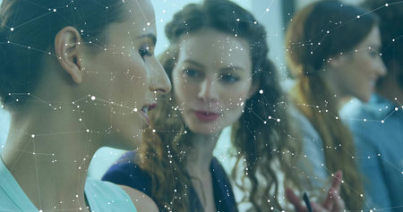 Collaborating professionals discussing data project at desk in office, with laptop, network overlay. Teamwork, innovation, connectivity, modernity, corporate, brainstorming, technologyの写真素材