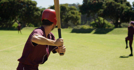 Baseball batter gripping wooden bat with helmet, watching baseball at park home plate with mound....