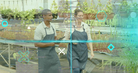 Walking nursery workers wearing aprons inspecting seedlings in greenhouse, with tablet, smartphone....