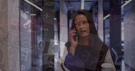 Talking businesswoman holding coffee cup, speaking on smartphone in modern office, with map overlay. Professional, corporate, modern, productivity, communication, technology, workspaceの写真素材