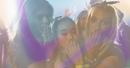 Laughing three friends covering mouths while dancing in club with wristbands, spotlights and haze. Celebration, nightlife, vibrant, energetic, social, dynamic, vividの写真素材