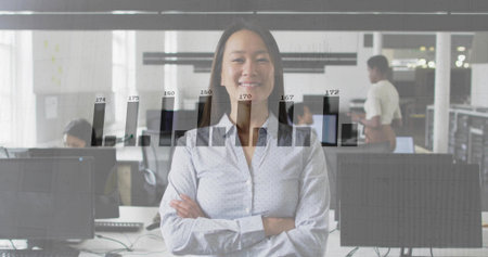Showing Asian woman wearing dotted top standing with arms crossed in office, with bar chart overlay. Professional, teamwork, data analysis, corporate, productivity, modern, business environmentの写真素材