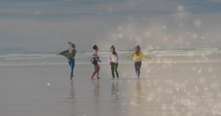Dancing four friends wearing casual jackets and pants in shallow surf at sandy beach with sparkles....