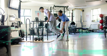 Performing client in light tee gray sweats lowering on parallel dip bars, trainer supporting ankle. Spotter, gym, workout, strength, coaching, equipment, balanceの写真素材