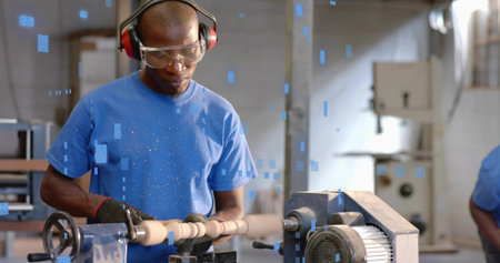 Operating lathe, mature Black man shaping spindle with shavings in shop, wearing goggles and gloves. Craftsmanship, industrial, manual, workshop, artisanal, woodworking, fabricationの写真素材