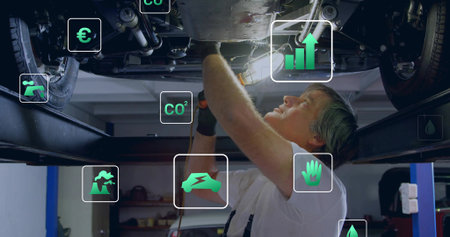 Drilling mechanic using power drill under vehicle chassis on lift in workshop, with overlay icons. Industrial, maintenance, technology, sustainability, innovation, engineering, automationの写真素材