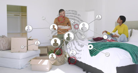 Man holding bowl of utensils and woman sitting on bed unpacking boxes, with digital overlay....