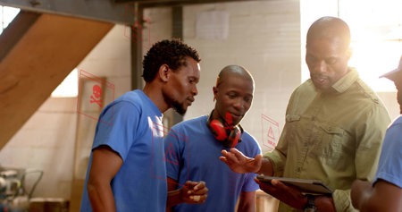 Examining tablet man in olive work shirt guiding blue tshirt workers in workshop with earmuffs. Industrial, teamwork, collaboration, engineering, machinery, workplace, trainingの写真素材